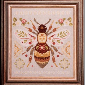May include: Cross-stitch artwork of a bee, framed in a wooden frame. The bee is detailed with brown, yellow, and tan colors, with floral and leaf accents. The background is a light gray fabric.