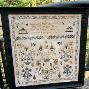 May include: A framed cross-stitch sampler on beige fabric featuring black and gold thread embroidery. The text reads: Loose me the Mighty Angel Cried, Why didst thou grasp Me so, Until thou bless me he replies, I will not let the go, Mary Ann Simmons, Finished this, Samy March, in 1840.