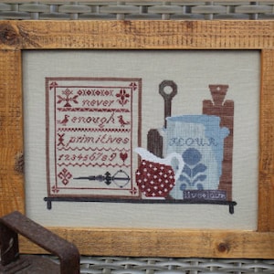 May include: A framed cross-stitch sampler with a rustic wooden frame. The sampler features a red and white design with the text "never enough primitives 123456789". The design also includes a pitcher, a bowl, and a spoon.