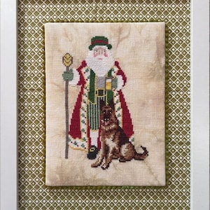 May include: Cross-stitch embroidery of a Santa Claus figure in a red and green suit holding a staff and a dog by his side. The background is a cream-colored fabric with a green and white diamond pattern.