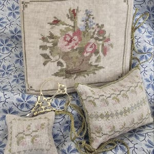 May include: Three embroidered pillow covers with floral designs. The largest pillow cover features a basket of flowers in shades of pink, green, and blue. The two smaller pillow covers feature a repeating floral pattern in shades of green and pink.