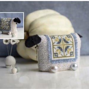 May include: A white and blue needle minder shaped like a sheep with black ears and a yellow and green geometric pattern on the back.