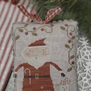 May include: Cross stitch pattern featuring a whimsical Santa Claus holding a candy cane and a snowman. The pattern is titled "Merry Old Soul" and is designed by Brenda Greves. The pattern is on a light gray linen fabric with a red and white gingham ribbon.