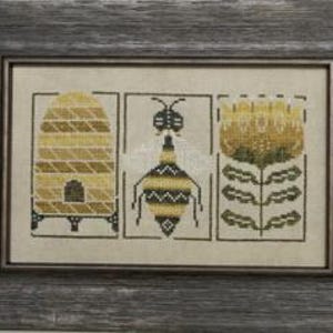 May include: Framed cross-stitch art featuring a beehive, a bee, and a flower. The artwork uses yellow, black, and green thread on a neutral background. The frame is a weathered gray wood. The overall theme is bees and nature.