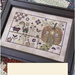 May include: Framed cross-stitch artwork featuring a whimsical autumn scene. A squirrel in overalls stands near a pumpkin house with a bird and flowers. The artwork is framed in a dark brown wooden frame, showcasing a detailed, colorful design with a fall theme.