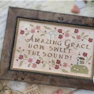 May include: A framed cross-stitch sampler with the words "Amazing Grace, How Sweet the Sound!" in brown thread. The sampler features floral and church motifs, framed in a rustic brown wooden frame. The design is by Brenda Gervais.