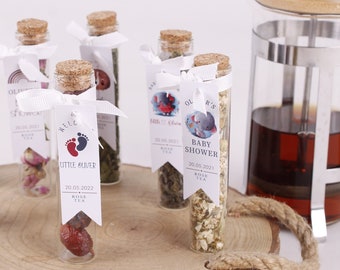 May include: A wooden tray with six small glass bottles filled with dried herbs and flowers. Each bottle has a white label with a different design and text, including "Baby Shower" and "Little  Monger". A silver and glass French press with a wooden lid is also on the tray.