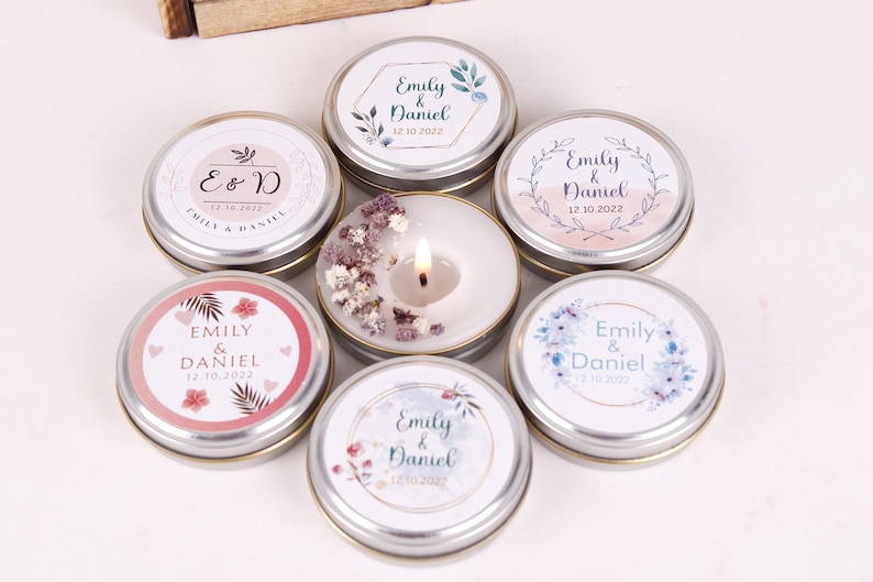 Peut inclure: Six petites bo&icirc;tes rondes en &eacute;tain avec couvercles, chacune pr&eacute;sentant un motif floral diff&eacute;rent et le texte "Emily & Daniel" avec une date de mariage. Les couvercles sont argent&eacute;s avec une bordure dor&eacute;e.