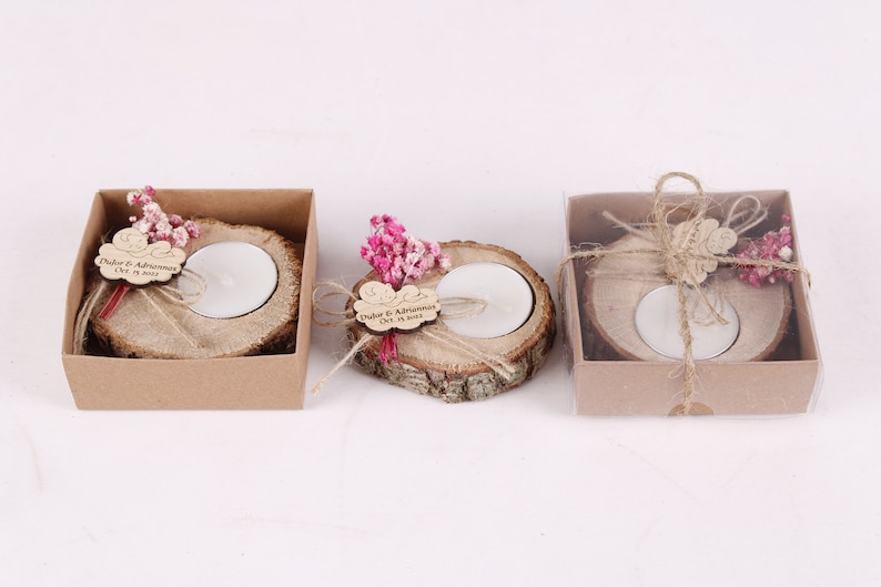 May include: Three small wooden candle holders with a tea light candle in each. The holders are decorated with dried flowers, twine, and a personalized wooden tag with the text "Duker & Adriana Oct 15, 2023".
