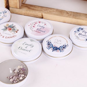 Peut inclure: Six bo&icirc;tes rondes en m&eacute;tal blanc contenant des bougies avec des motifs floraux et les noms "Emily & Daniel" ainsi que la date "12.10.2022".