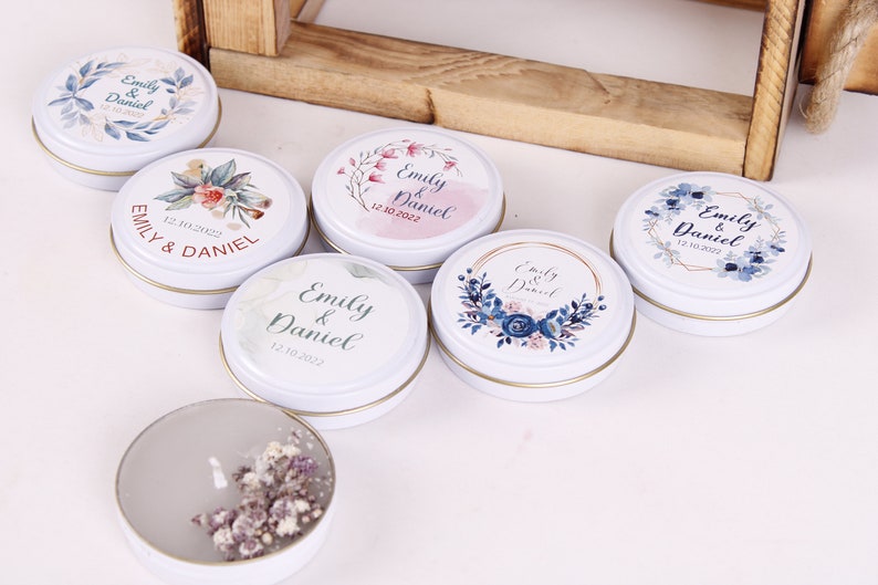 Peut inclure: Six bo&icirc;tes rondes en m&eacute;tal blanc contenant des bougies avec des motifs floraux et les noms "Emily & Daniel" ainsi que la date "12.10.2022".