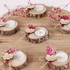 May include: Six small wooden candle holders with a tea light candle in each. Each holder is decorated with a small piece of wood with the text "Duygu & Adnan" and a small bouquet of pink flowers.