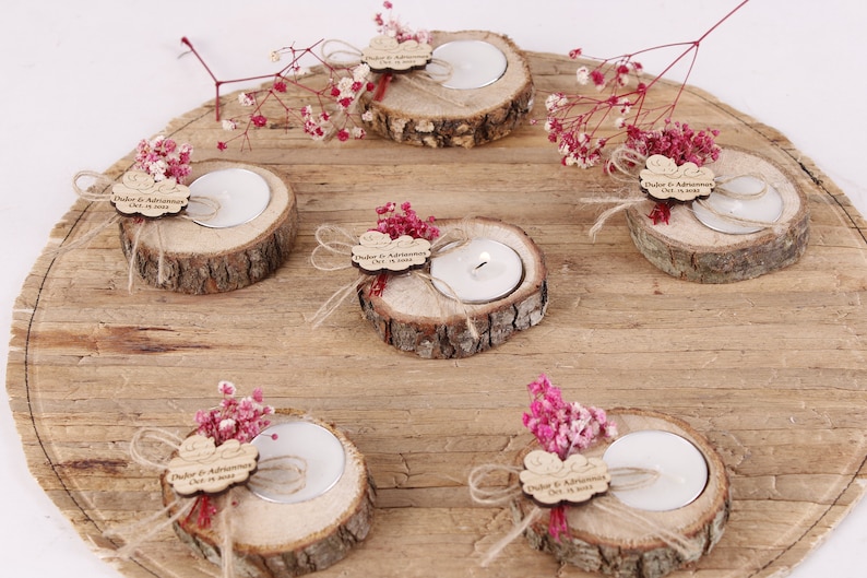 May include: Six small wooden candle holders with a tea light candle in each. Each holder is decorated with a small piece of wood with the text "Duygu & Adnan" and a small bouquet of pink flowers.