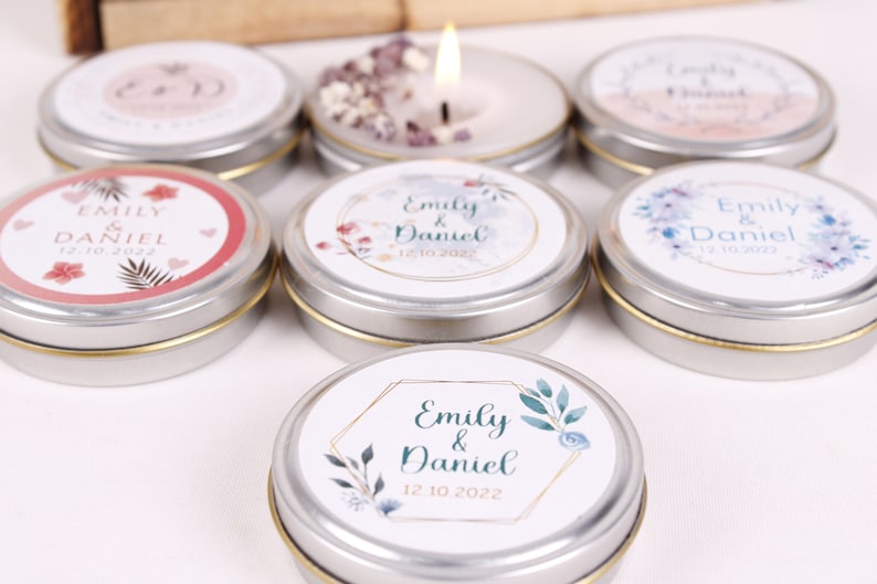 Peut inclure: Assortiment de petites bo&icirc;tes rondes en argent avec des &eacute;tiquettes blanches orn&eacute;es de motifs floraux et du texte "Emily & Daniel" avec une date de mariage. Les bo&icirc;tes contiennent de petites bougies.