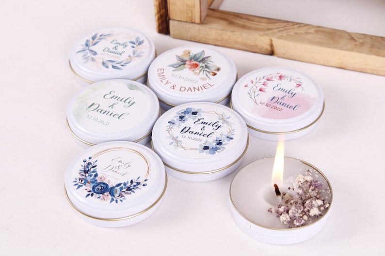 Peut inclure: Assortiment de petites bo&icirc;tes rondes blanches avec des motifs floraux et le texte "Emily & Daniel" et une date. Les bo&icirc;tes contiennent de petites bougies blanches.