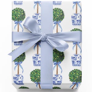 May include: A wrapped gift with a white background featuring a repeating pattern of green topiary trees in blue and white pots. The gift is tied with a light blue satin ribbon and bow.