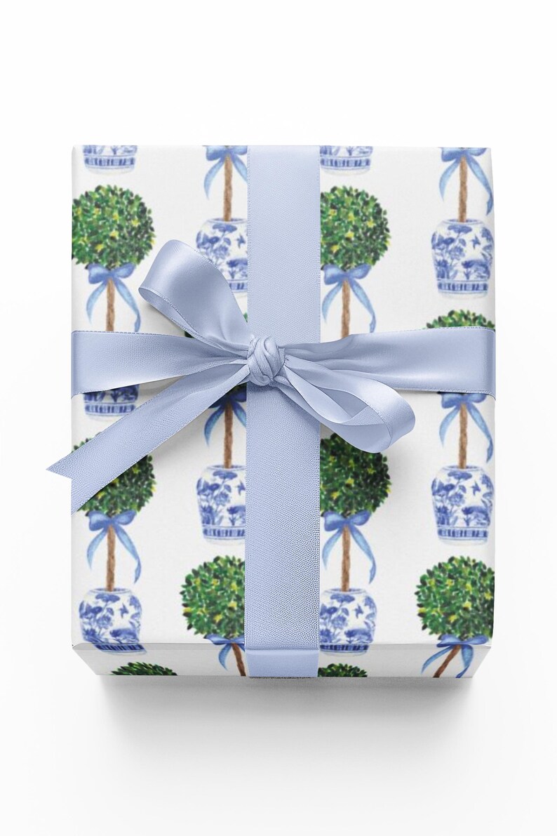 May include: A wrapped gift with a white background featuring a repeating pattern of green topiary trees in blue and white pots. The gift is tied with a light blue satin ribbon and bow.