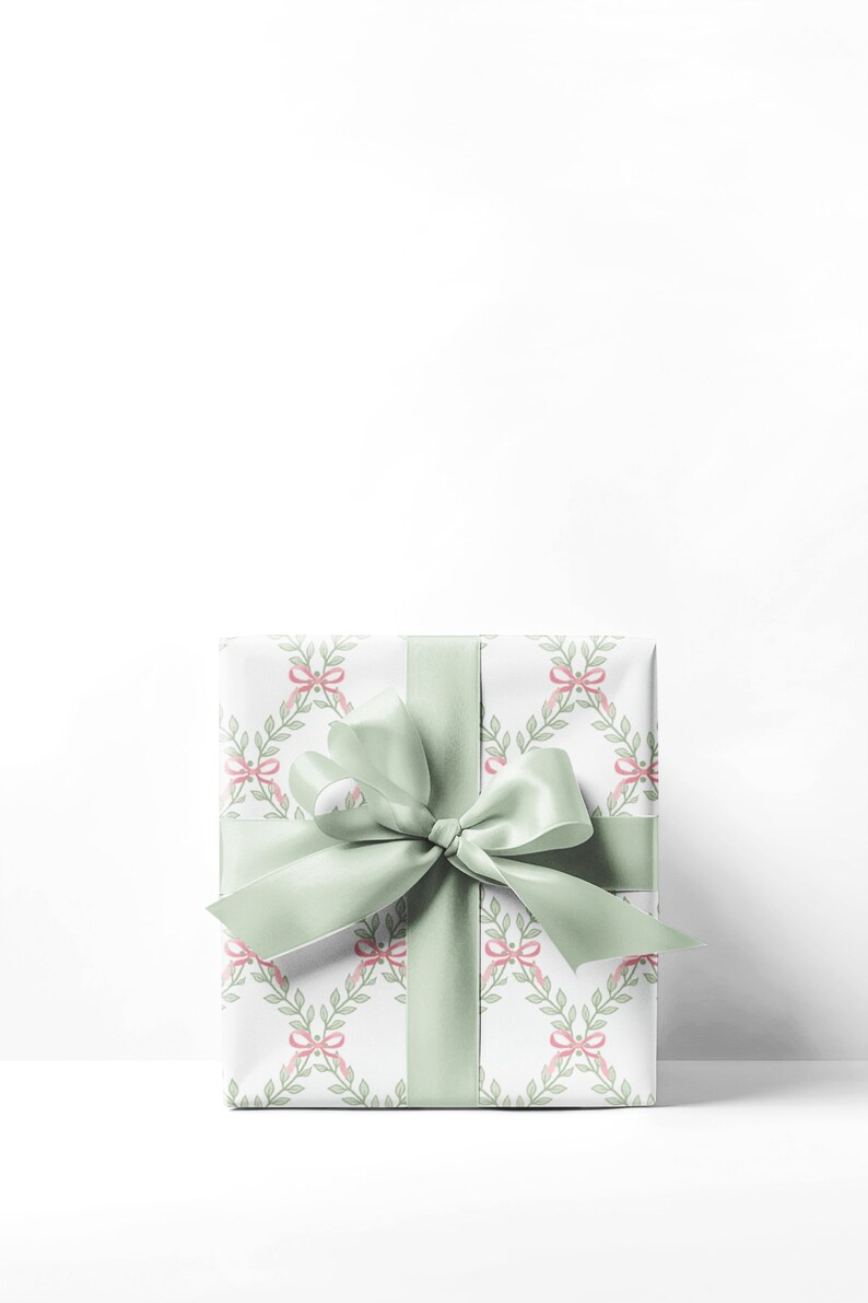 May include: A white gift box with a green ribbon and a pattern of pink bows and green leaves.