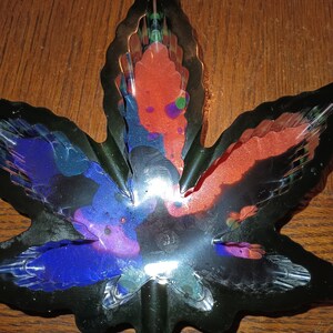 May include: A black metal leaf-shaped dish with a multi-colored resin design. The resin is a mix of blue, green, purple, and orange colors.