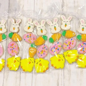 May include: Six individual cellophane bags filled with Easter-themed sugar cookies. Each bag contains a bunny, carrot, egg, and chick cookie. The cookies are decorated with pastel colors and sprinkles.