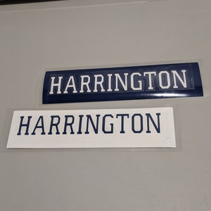 May include: Two white rectangular name tags with the word "HARRINGTON" printed in blue letters. The top tag has a blue background.