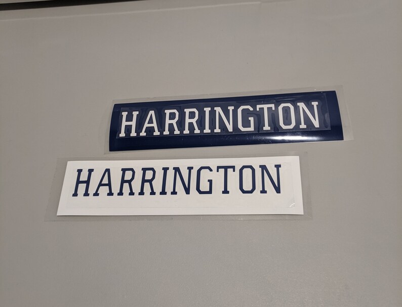 May include: Two white rectangular name tags with the word "HARRINGTON" printed in blue letters. The top tag has a blue background.