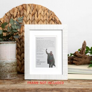 May include: A white framed print with a quote from the movie "The Breakfast Club" and a picture of the character John Bender raising his fist in the air. The quote reads: "We accept the fact that we had to sacrifice a whole Saturday in detention for the sake of our education. But in the course of this last week, we've come to realize that each of us is a brain, and an athlete, and a basket case, a princess, and a criminal. Does that answer your question?" The print is on a wooden table with a potted plant and a piece of driftwood.