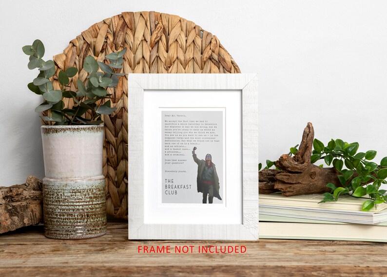 May include: A white framed print with a quote from the movie "The Breakfast Club" and a picture of the character John Bender raising his fist in the air. The quote reads: "We accept the fact that we had to sacrifice a whole Saturday in detention for the sake of our education. But in the course of this last week, we've come to realize that each of us is a brain, and an athlete, and a basket case, a princess, and a criminal. Does that answer your question?" The print is on a wooden table with a potted plant and a piece of driftwood.