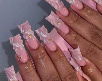 May include: Pink and white long, sculpted, and pointed acrylic nails with gold glitter accents.
