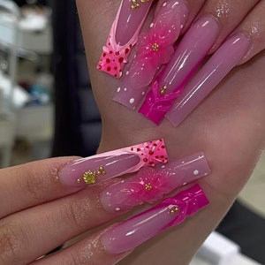 May include: Long, pink and white acrylic nails with 3D flower and seashell designs. The nails are decorated with pink and white polka dots.