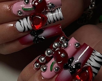 May include: Close-up of a hand with long, red, pink, and black nails decorated with cherries, stars, and zebra print.