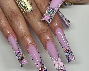 May include: Long, pink, stiletto nails with silver glitter and rhinestones. The nails are decorated with pink flowers and bows.