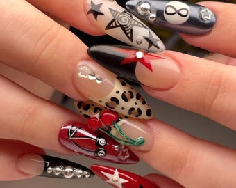 May include: Close-up of several long, almond-shaped nails with different designs. One nail has a red and black cherry design, another has a leopard print, and another has a black and white star design with the infinity symbol.