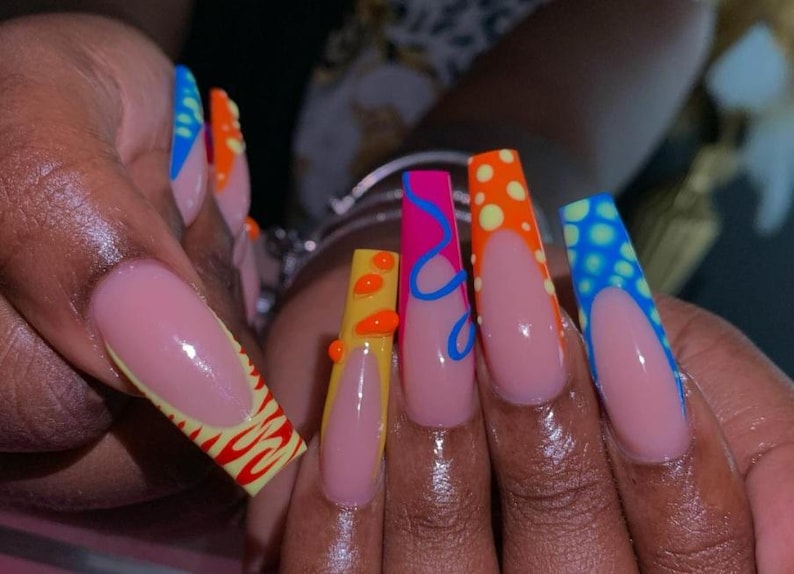 May include: Long, pink, almond-shaped nails with colorful designs. The nails are painted with a light pink base and have different designs on each nail, including yellow, orange, blue, and pink.