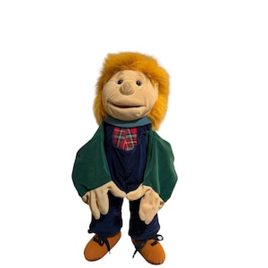 May include: A plush puppet featuring a tan face with freckles, bright orange hair, and a teal collar. The puppet wears a dark blue jumpsuit with a red and green plaid chest panel, green sleeves, and tan shoes with black laces on its hands and feet.