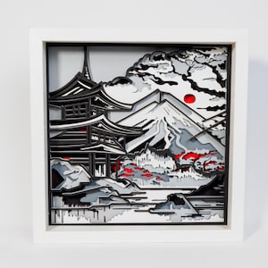 Könnte beinhalten: Gerahmtes, geschichtetes Papierkunstwerk, das eine japanische Landschaft darstellt. Das Kunstwerk zeigt eine Pagode, den Berg Fuji und eine rote Sonne. Die Farbpalette umfasst Schwarz, Weiß, Grau und Rot, was einen auffälligen Kontrast erzeugt. Das Stück ist in einem weißen Rahmen eingefasst.