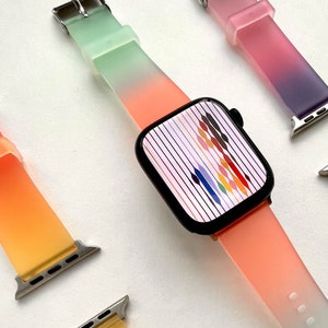 May include: Four colorful silicone watch bands with a gradient color effect. The bands are in shades of green, pink, purple, and orange. The bands are designed for Apple Watches.