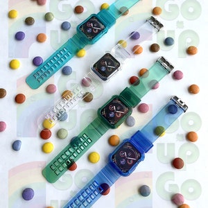 May include: Four clear and blue Apple Watch bands with clear cases. The bands are made of a flexible, translucent material with a grid pattern. The cases are designed to protect the watch face. The bands are arranged in a circle on a white surface with colorful candy.