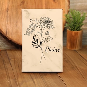 Puede incluir: Un lienzo rectangular con un patr&oacute;n similar al m&aacute;rmol presenta un dise&ntilde;o floral negro y el nombre "Claire". La obra de arte incluye dibujos detallados de flores, hojas y tallos. El lienzo se exhibe sobre una superficie de madera.