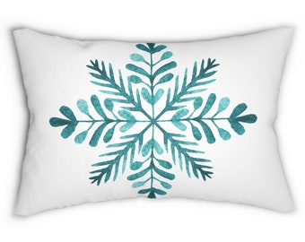 May include: A white throw pillow with a teal blue snowflake design. The snowflake is stylized and has a watercolor effect.