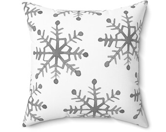 Puede incluir: Almohada blanca con un patrón de copo de nieve gris.