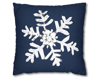 May include: A square navy blue decorative pillow featuring a large white snowflake design. The snowflake has a hand-painted appearance with textured details. This winter-themed pillow adds a touch of seasonal charm to any room.