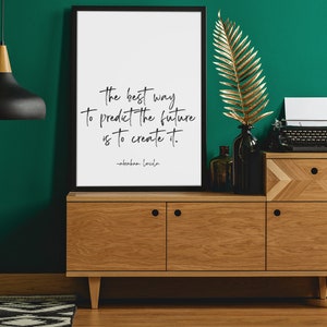 May include: A framed print with a quote by Abraham Lincoln: "The best way to predict the future is to create it." The print is hanging on a teal wall above a wooden cabinet with a gold leaf branch in a vase.