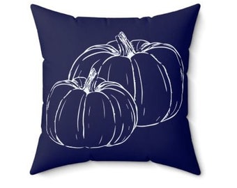 May include: Square throw pillow with a navy blue background and a white line drawing of two pumpkins. The pumpkins are detailed with vertical lines and stems, creating a fall or harvest theme.