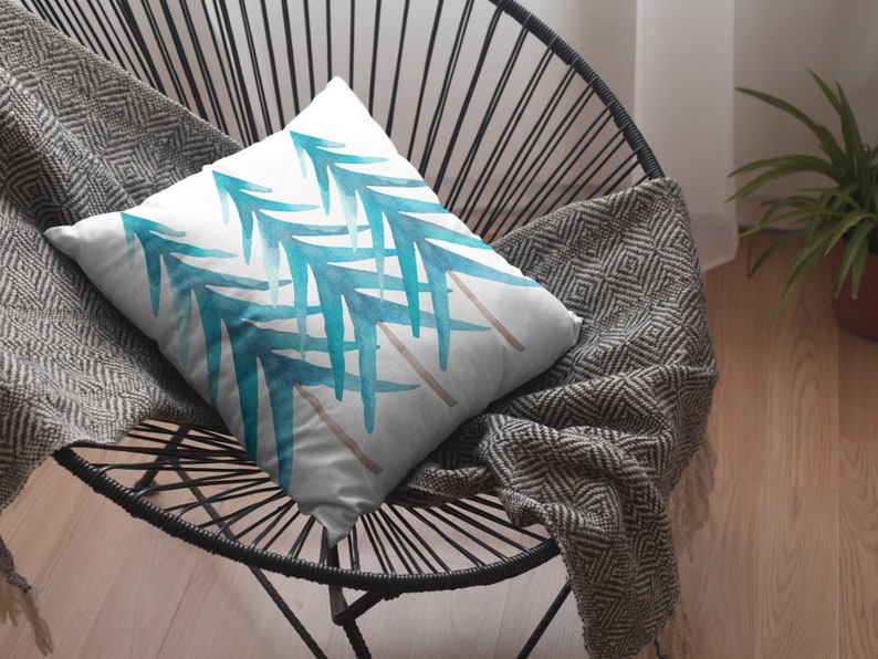 Pode incluir: Uma almofada quadrada com fundo branco e um desenho em aquarela de folhas azul-esverdeadas. A almofada est&aacute; em uma cadeira preta com um cobertor cinza estampado.