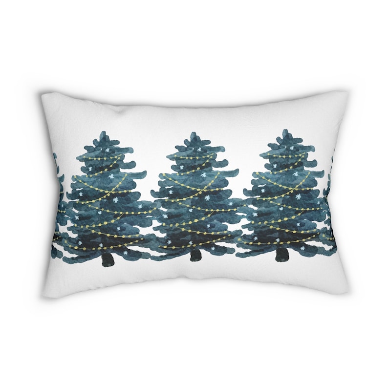 May include: A white rectangular pillow with a blue and gold watercolor design of three Christmas trees with lights and snowflakes.