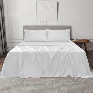 Puede incluir: Un juego de sábanas blancas en una cama con dos fundas de almohada a juego. Las sábanas están cuidadosamente dispuestas, con un aspecto liso y sin arrugas. La cama está contra un cabecero gris claro y una alfombra estampada.