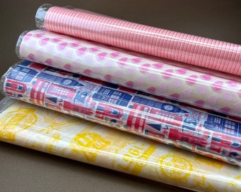 May include: Four rolls of decorative wrapping paper with different patterns. The top roll is pink and white striped, the second roll is pink and white with a heart pattern, the third roll is red, white, and blue with a London theme, and the bottom roll is yellow with a vintage stamp design.