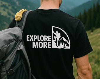 Könnte beinhalten: Schwarzes T-Shirt mit den Worten "EXPLORE MORE" und einer weißen Grafik eines Bergsteigers. Die Person trägt einen Rucksack und steht vor einer Bergkette.