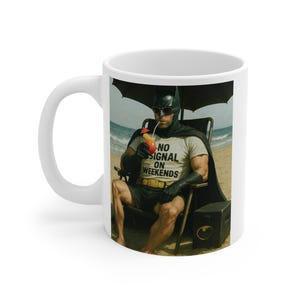 May include: White ceramic coffee mug featuring a humorous image of Batman relaxing on a beach, wearing sunglasses and a t-shirt that reads "NO SIGNAL ON WEEKENDS." The mug has a black handle and a glossy finish.